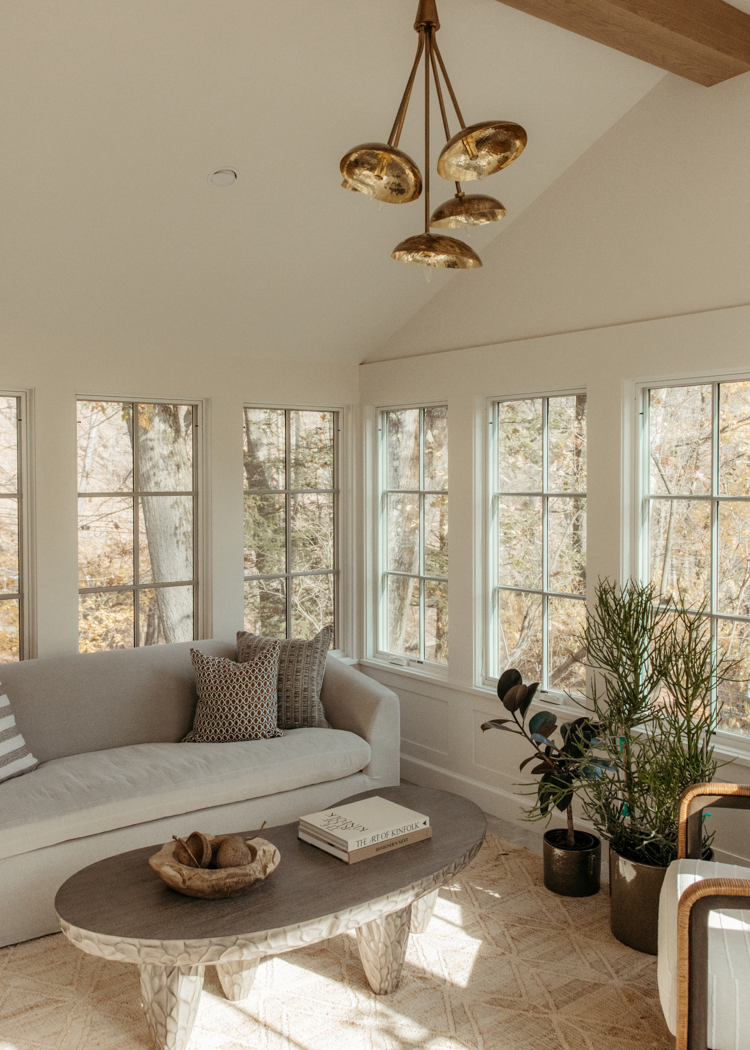A designed sitting room with a couch, coffee table, bay windows, and plants.